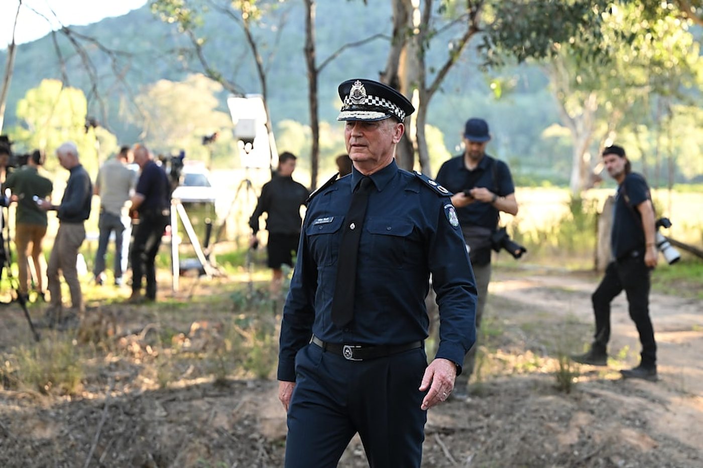 The Chief Commissioner walks through bushland trailed by a media pack.