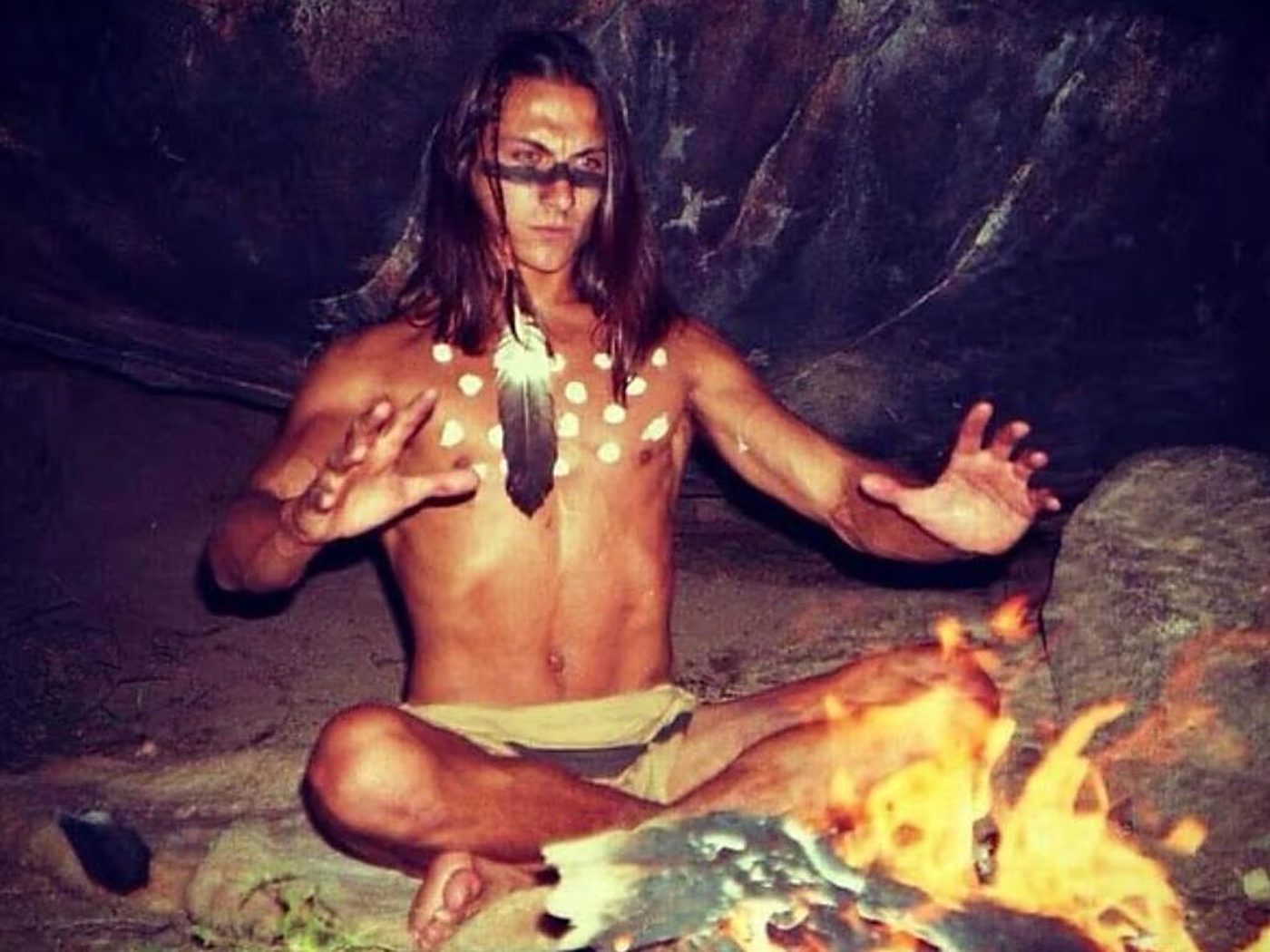 A young Freeman in face paint beside a campfire in a cave.