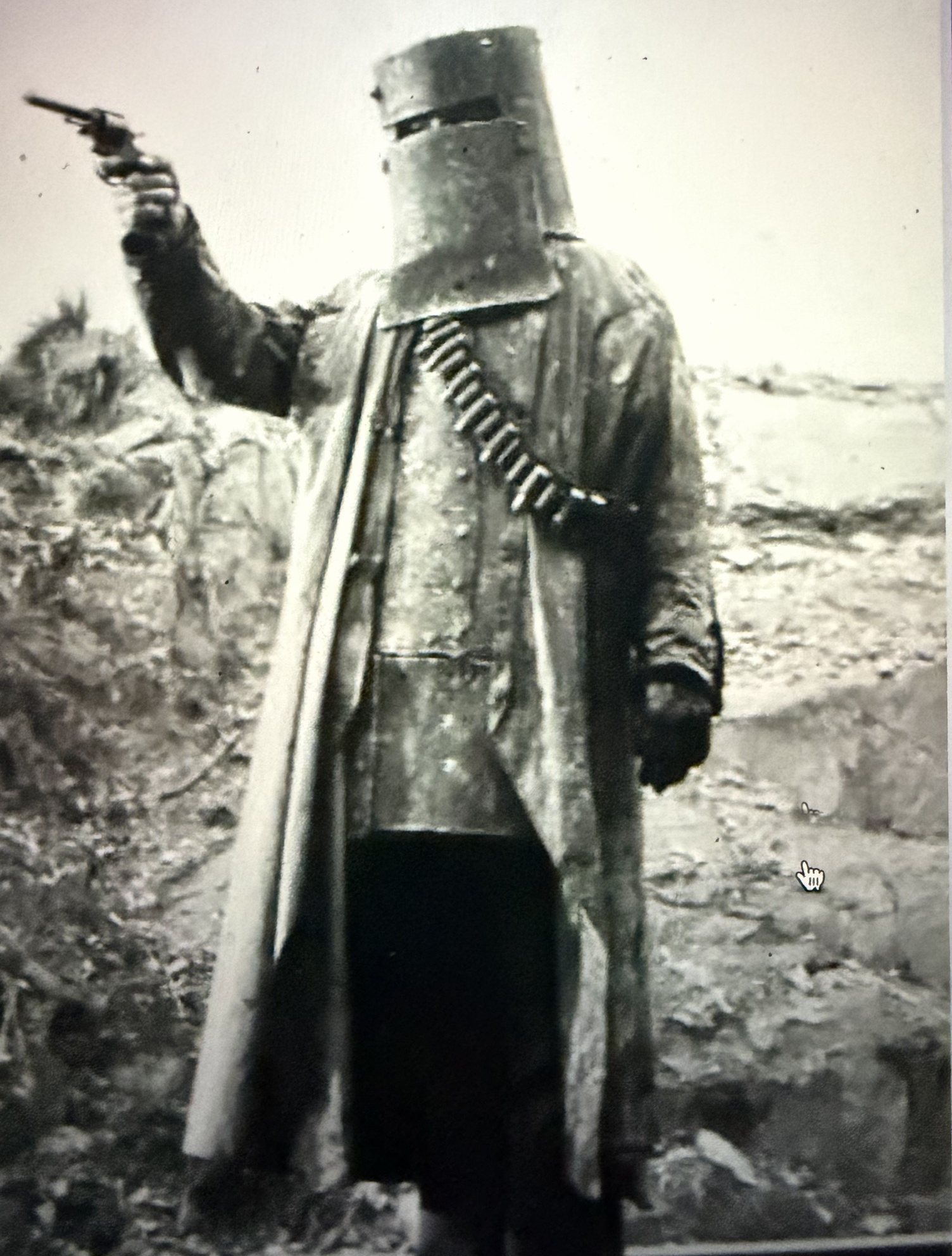 A figure in Kelly Gang armour, revolver raised, against open country.