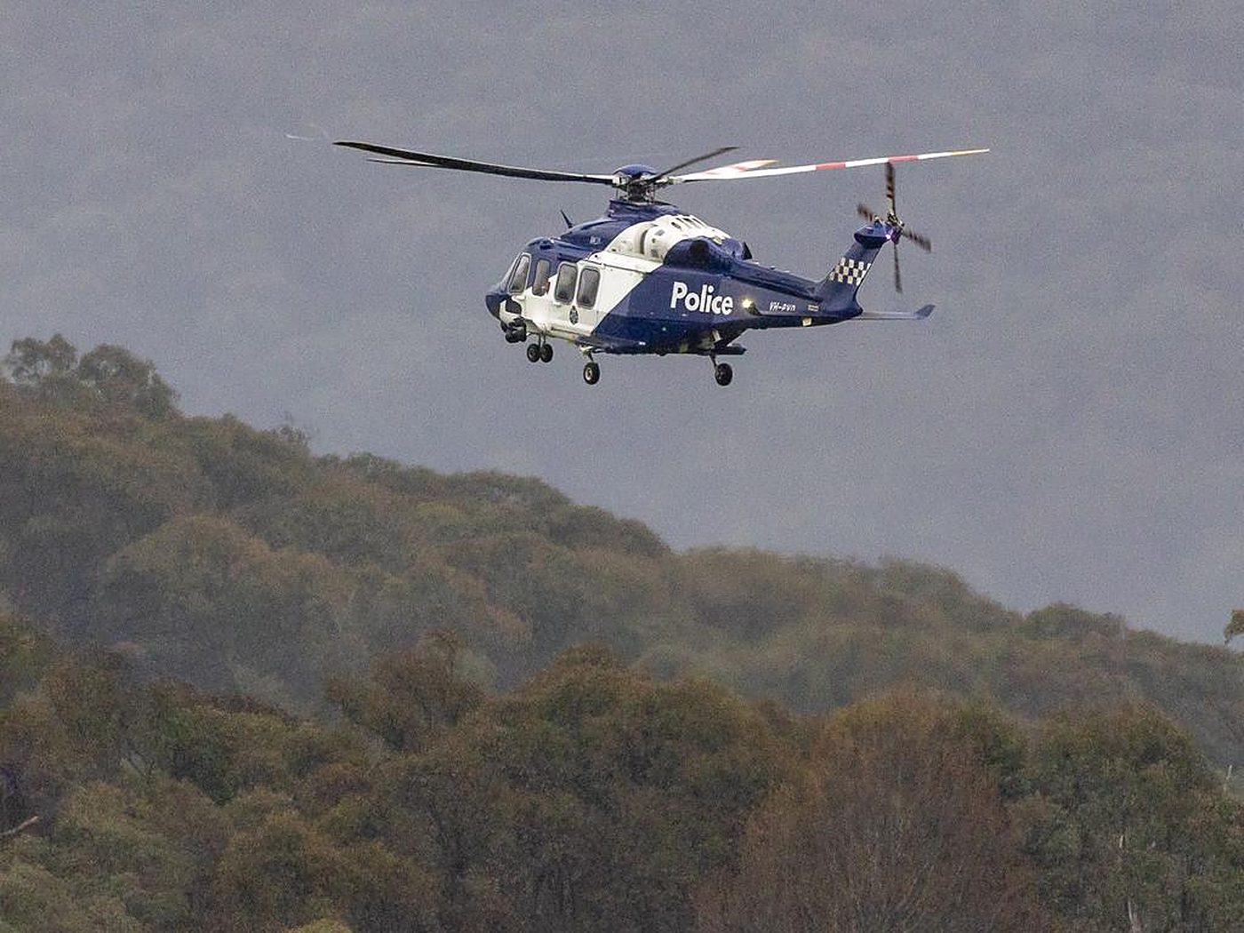 A police helicopter hanging over dark forested ranges.