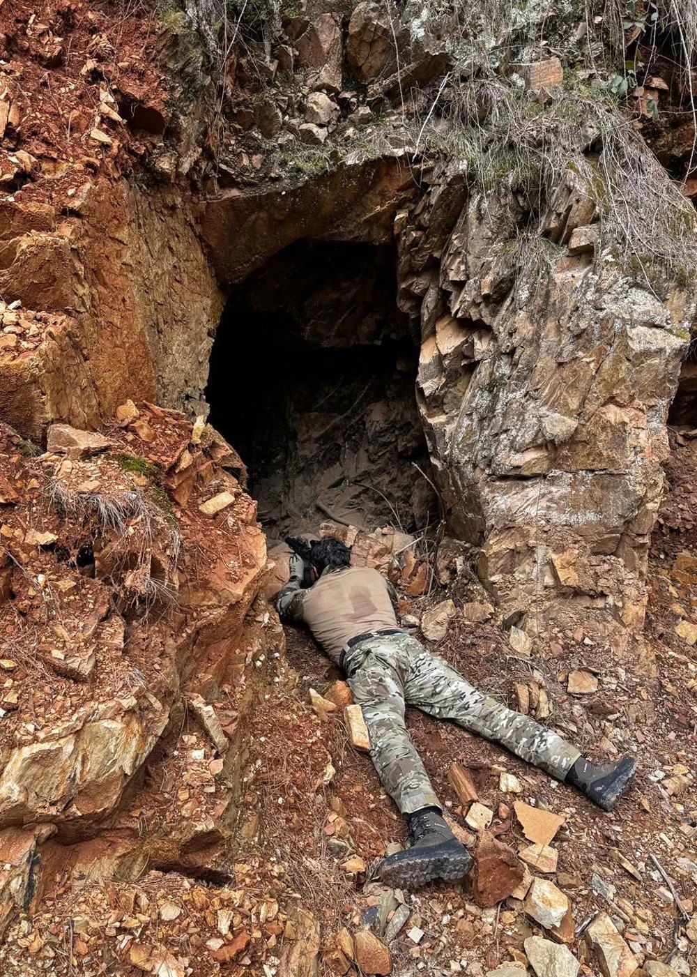 An officer prone in the rubble at a red-earth mine adit, pistol trained into the opening.
