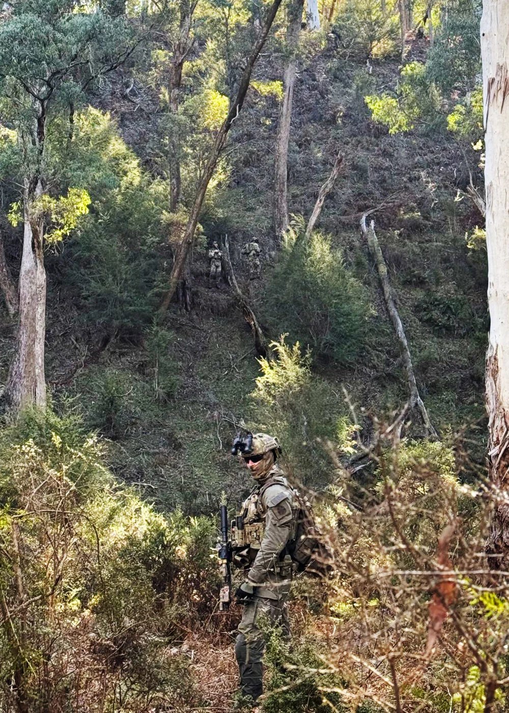 Three officers strung down a steep bush gully in sweep formation.