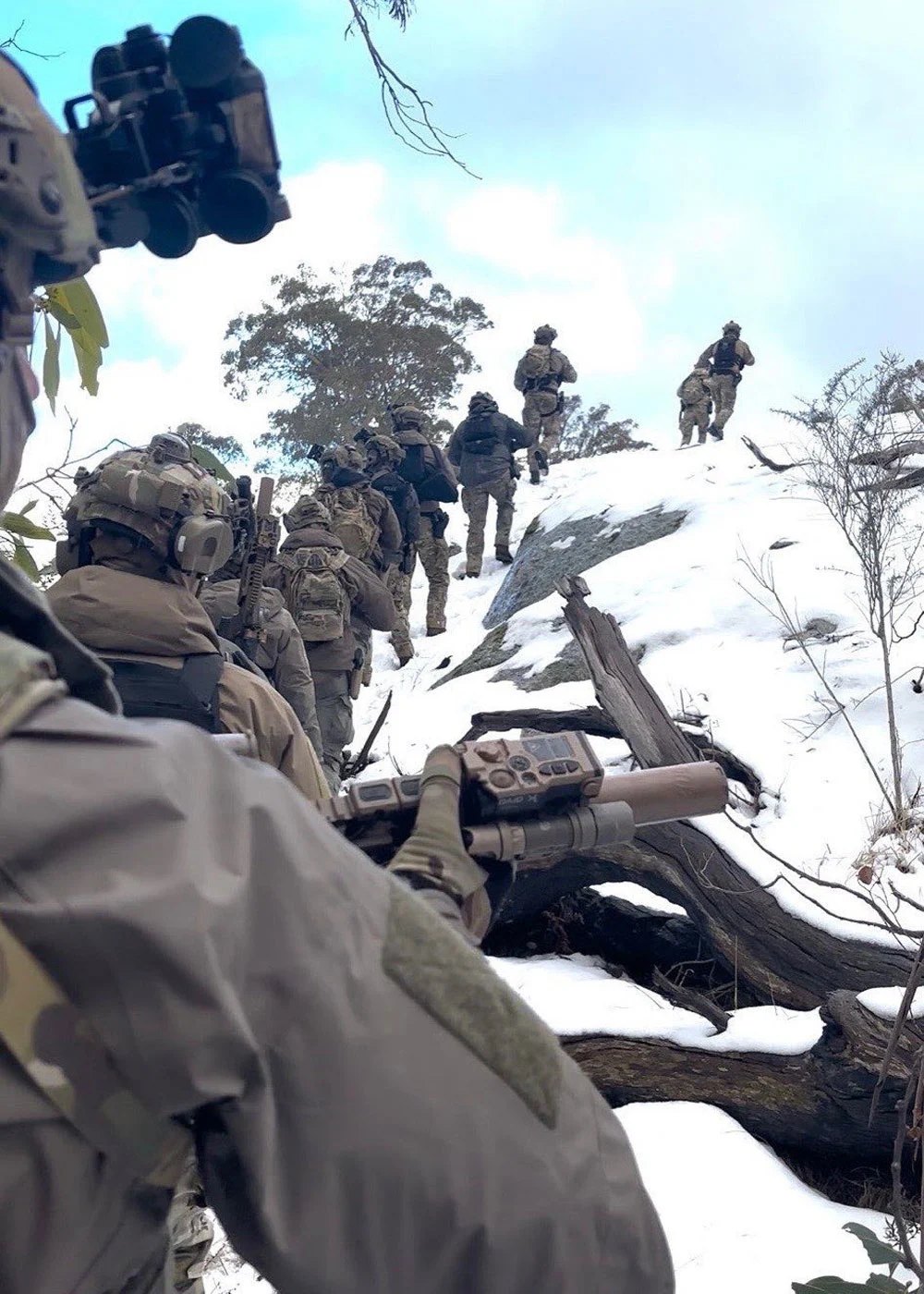 A tactical column ascending a snow-covered ridge in single file.
