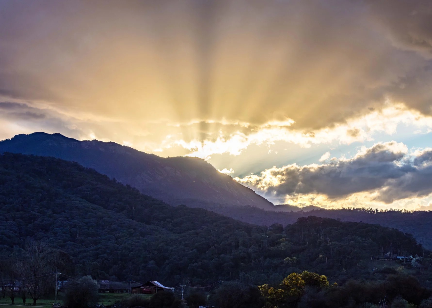 Evening light breaking through cloud over the ranges, rays falling across the valley.