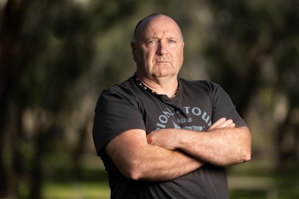 Bruce Evans with arms crossed beneath gum trees.