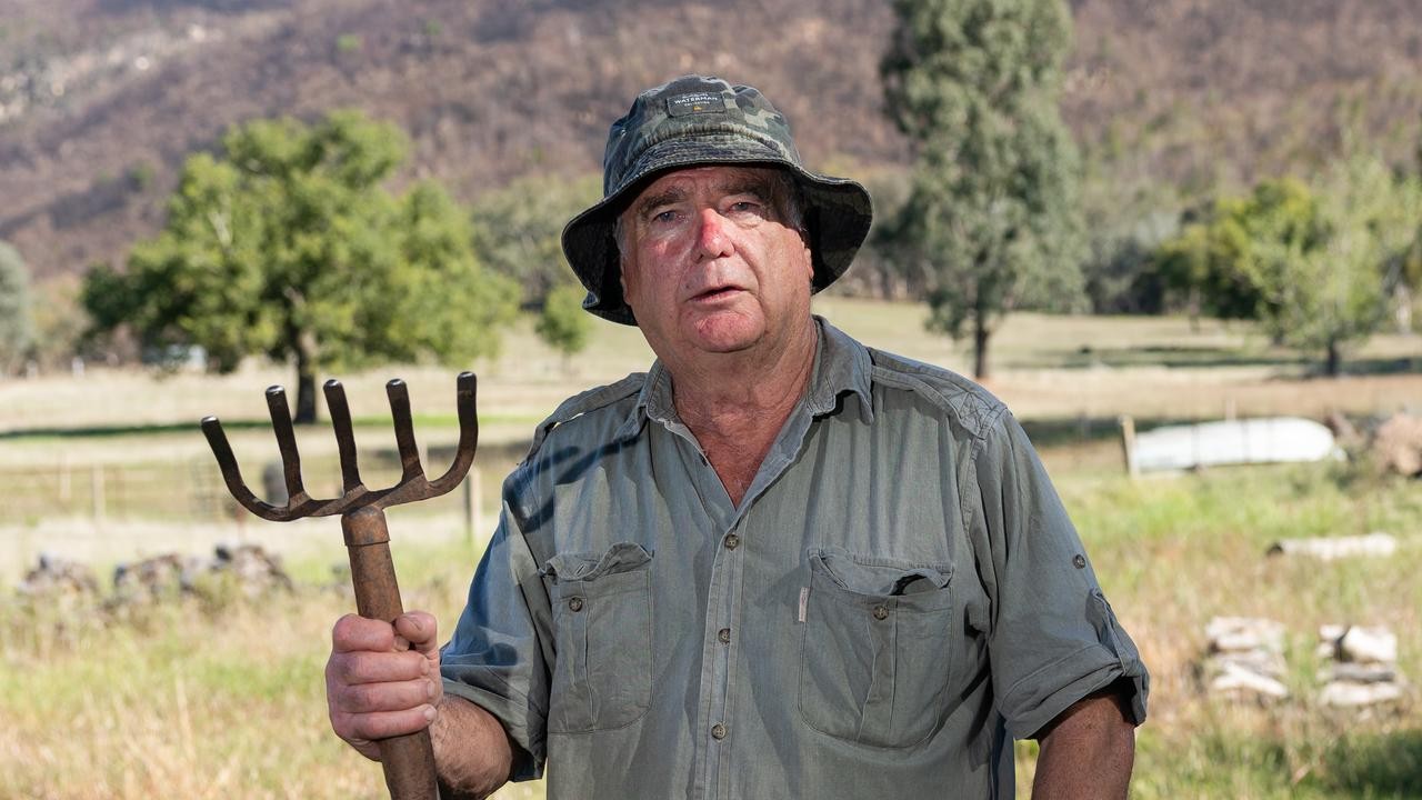 Neil Sutherland on his property, holding an old pitchfork, burnt ranges behind him.