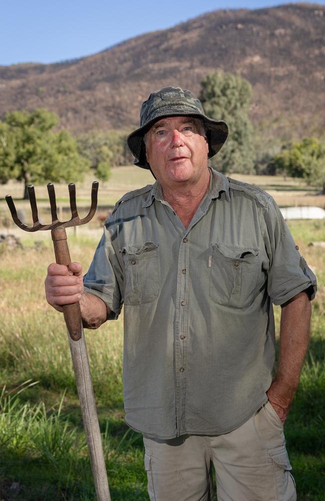 Richard Sutherland in his paddock with a pitchfork, a fire-scarred hillside behind him.