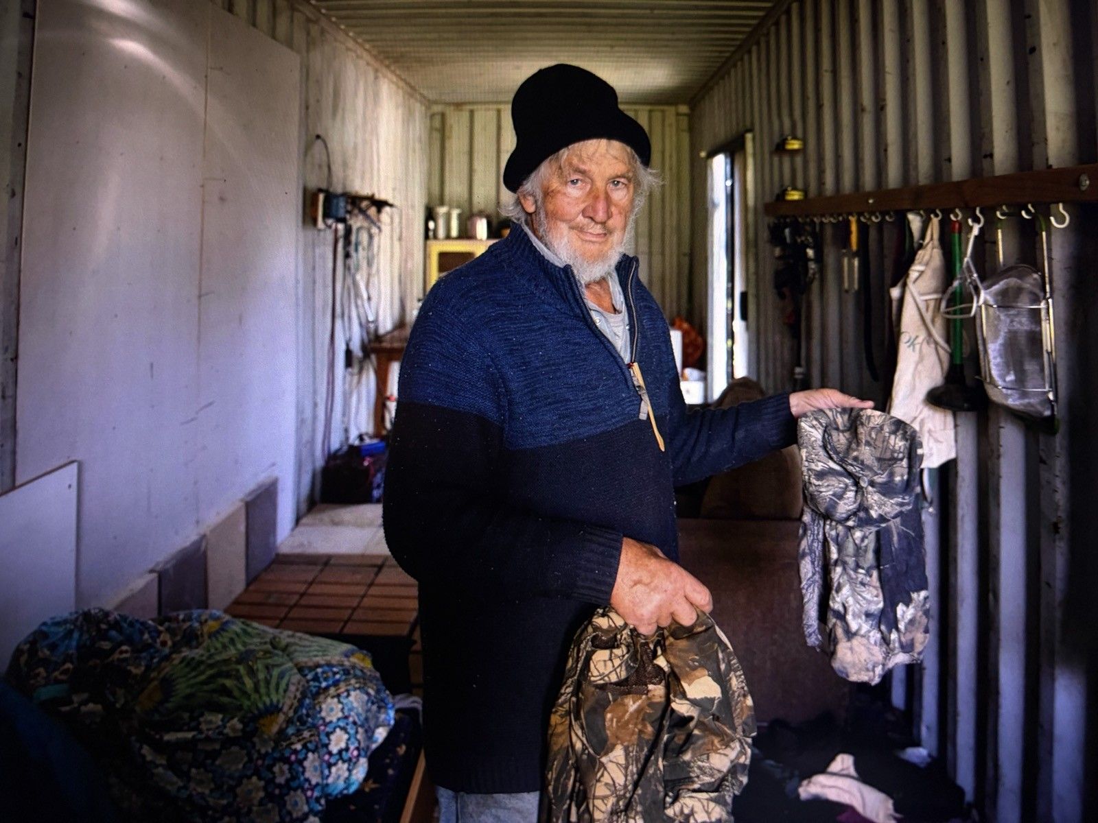 Richard Sutherland inside the shipping container, holding the camouflage clothing left behind.