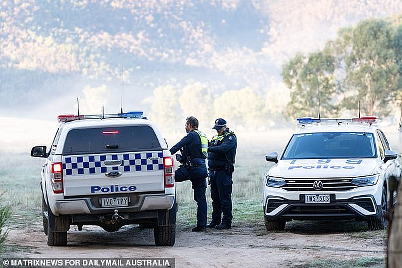 Police vehicles at a misty dawn roadblock beneath the ranges.