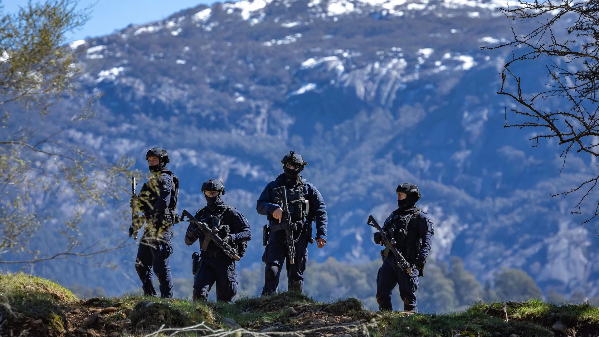 Four tactical officers on a ridge line beneath the snowbound face of Mount Buffalo.